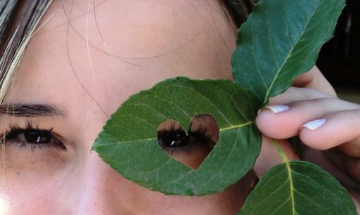 Eye looking through a heart shaped hole in a leaf